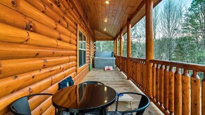 A wooden log cabin with a covered porch, a table with chairs, and a view of the surrounding forest. - Lykke Lodge (Pigeon Forge)