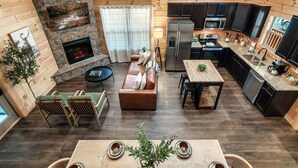 A cozy cabin interior with a stone fireplace, a living area with a sofa and chairs, a dining table, and a kitchen with modern appliances. - Lykke Lodge (Pigeon Forge)