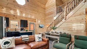 A wooden interior with a sofa, chairs, a staircase, and a kitchen area. - Lykke Lodge (Pigeon Forge)