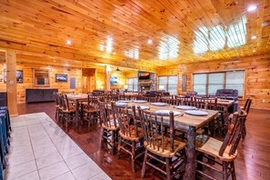 Ein rustikales Holzhaus-Interieur mit mehreren Esstischen und Stühlen, einem Steinkamin und einem an der Wand befestigten Fernseher.