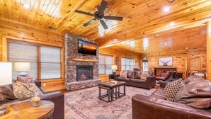 A cozy cabin interior with a stone fireplace, leather furniture, and a ceiling fan. - Mayes Landing (Pigeon Forge)