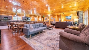 A spacious living area with wooden floors, a large sofa, a coffee table, and a fireplace. - Mayes Landing (Pigeon Forge)