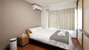 A hotel room with a bed, an air conditioning unit, a bedside table with a tissue box, and a window with curtains. - Private whole-house stay in a quiet area of Shinoro, Sapporo. 3 bedrooms, up to 6 guests (札幌市)