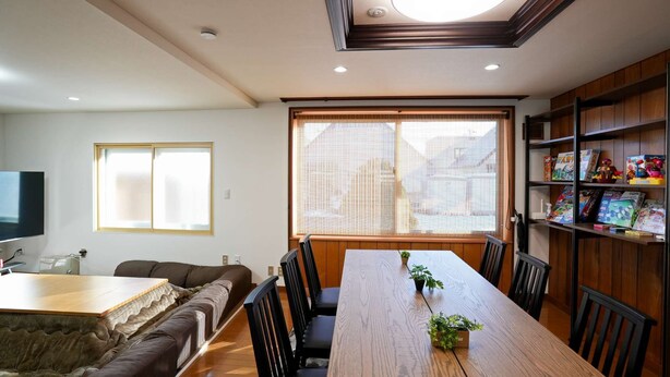 A dining area with a wooden table, chairs, a sofa, and a bookshelf with books and games. - Private whole-house stay in a quiet area of Shinoro, Sapporo. 3 bedrooms, up to 6 guests (札幌市)
