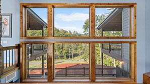 A multi-level wooden structure with large windows offering views of a landscaped area and trees. - Riverside Retreat in Ellijay GA (Ellijay)