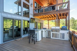 Eine moderne Außenküche mit Grill, Barhocker und einer Holzterrasse.