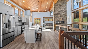 A modern kitchen with a central island, a stone fireplace, and large windows. - Riverside Retreat in Ellijay GA (Ellijay)