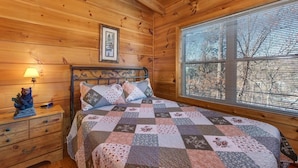 Un dormitorio tipo cabaña de madera con cama, mesita de noche, lámpara y ventana con persianas.