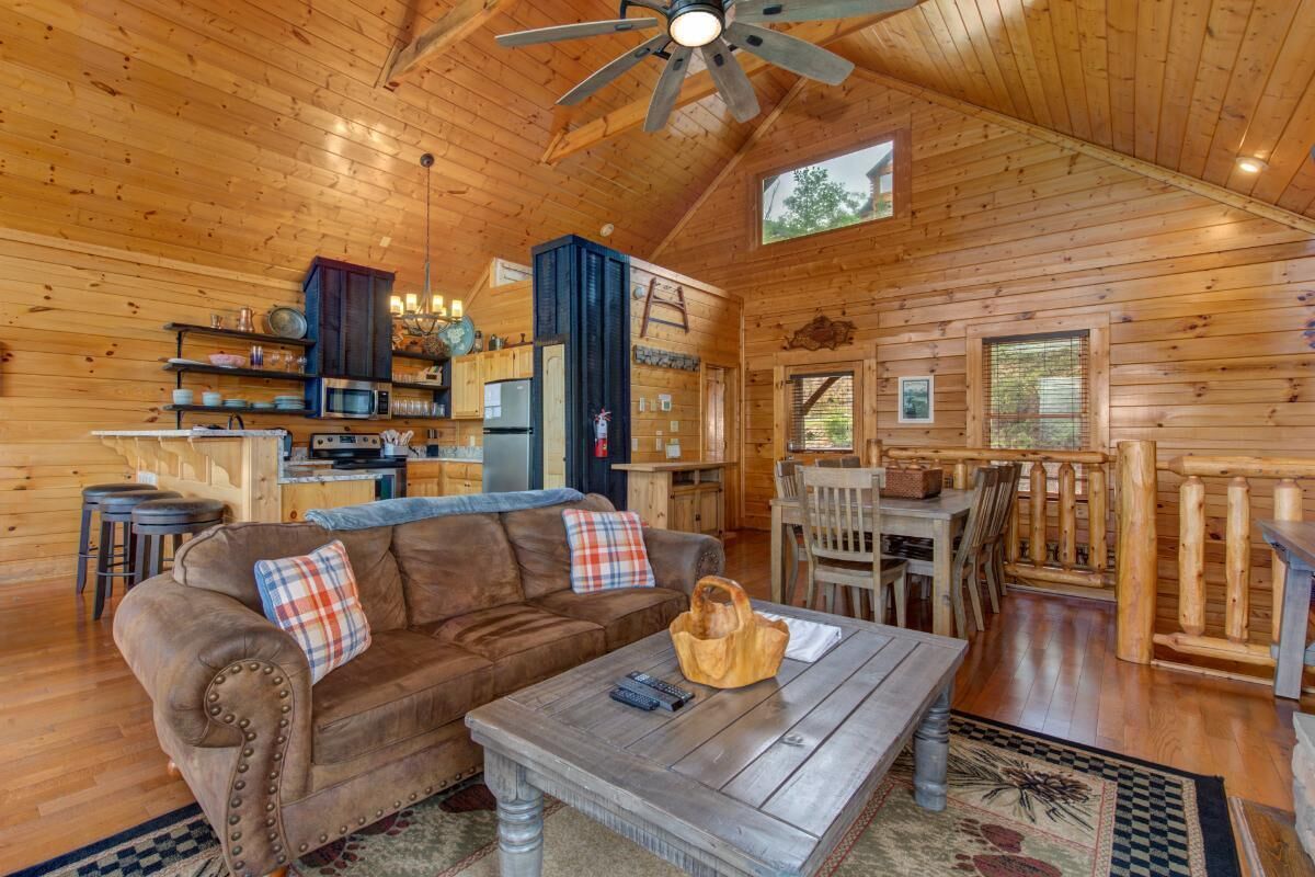 A wooden cabin interior with a dining area, kitchen, and a sofa with pillows.