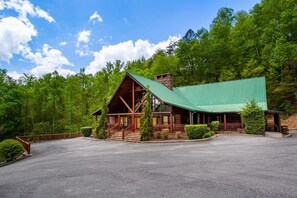 A lodge with a green roof, wooden exterior, and a spacious parking area. - Poolin' Around (Pigeon Forge)