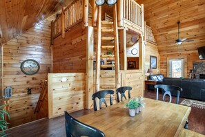 A wooden cabin interior with a dining area, a fireplace, a loft bedroom, and a living room. - Poolin' Around (Pigeon Forge)