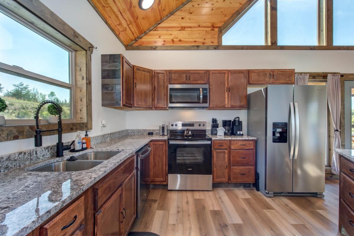 A kitchen with wooden cabinets, stainless steel appliances, granite countertops, and a large window.