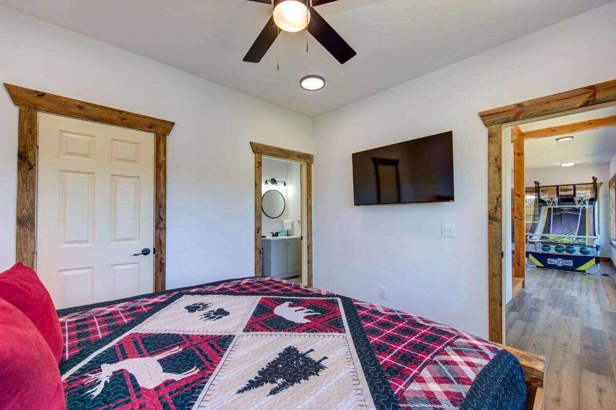 A bedroom with a bed, a ceiling fan, a mounted TV, and a door leading to another room.