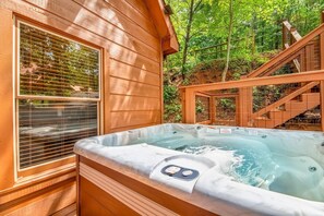 A wooden cabin with a hot tub, a window with blinds, and a staircase leading to a deck. - Z - The Overlook (Sevierville)