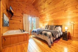 A wooden cabin bedroom with a bed, a nightstand, a lamp, a window, and a wooden wall. - Z - The Overlook (Sevierville)