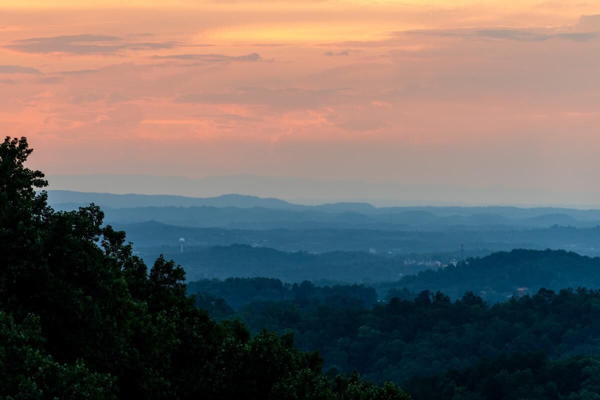 A panoramic view of a mountainous landscape with dense forestation in the foreground and distant hills.