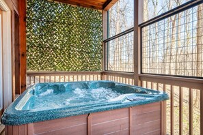 A hot tub in a wooden deck area with a lattice wall and large windows. - Smoky Summit Stays (Sevierville)