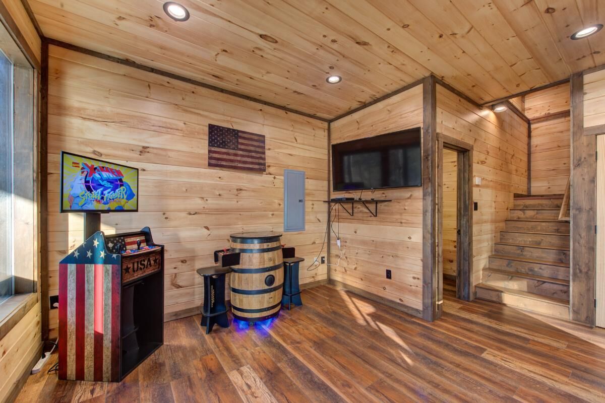 A wooden interior with a barrel, a TV, and a USA-themed arcade machine.