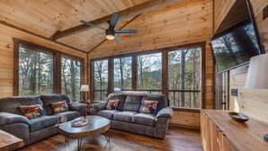 A cabin interior with a wooden ceiling, large windows, a sofa set, a coffee table, and a wooden bar area. - Bearfoot Splash Hideaway (Sevierville)