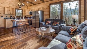 A log cabin interior with a kitchen, dining area, and seating with a view of the forest. - Bearfoot Splash Hideaway (Sevierville)