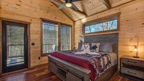 A wooden cabin bedroom with a bed, two windows, a ceiling fan, and a nightstand. - Bearfoot Splash Hideaway (Sevierville)
