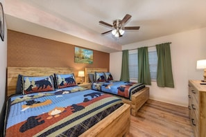 A bedroom with two beds, a ceiling fan, a painting, and green curtains. - Cs Creekside Condo (Gatlinburg)