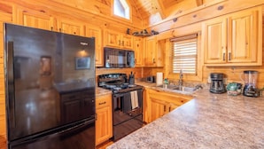 A kitchen with wooden cabinets, a black refrigerator, a stove, a microwave, and a coffee maker. - Roudys Roost (Pigeon Forge)