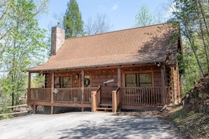 A wooden cabin with a porch, a chimney, and a welcome sign. - Roudys Roost (Pigeon Forge)