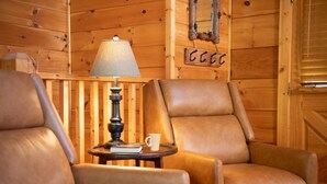 A wooden cabin interior with two leather armchairs, a small table with a lamp, and a cup. - Roudys Roost (Pigeon Forge)