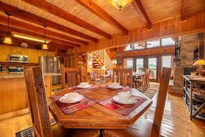 A wooden cabin interior with a dining table set for four, a kitchen with modern appliances, and a staircase leading to an upper level. - Psalm 2705 (Sevierville)