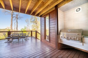 A covered outdoor deck with a grill, wooden furniture, and a view of trees. - Psalm 2705 (Sevierville)