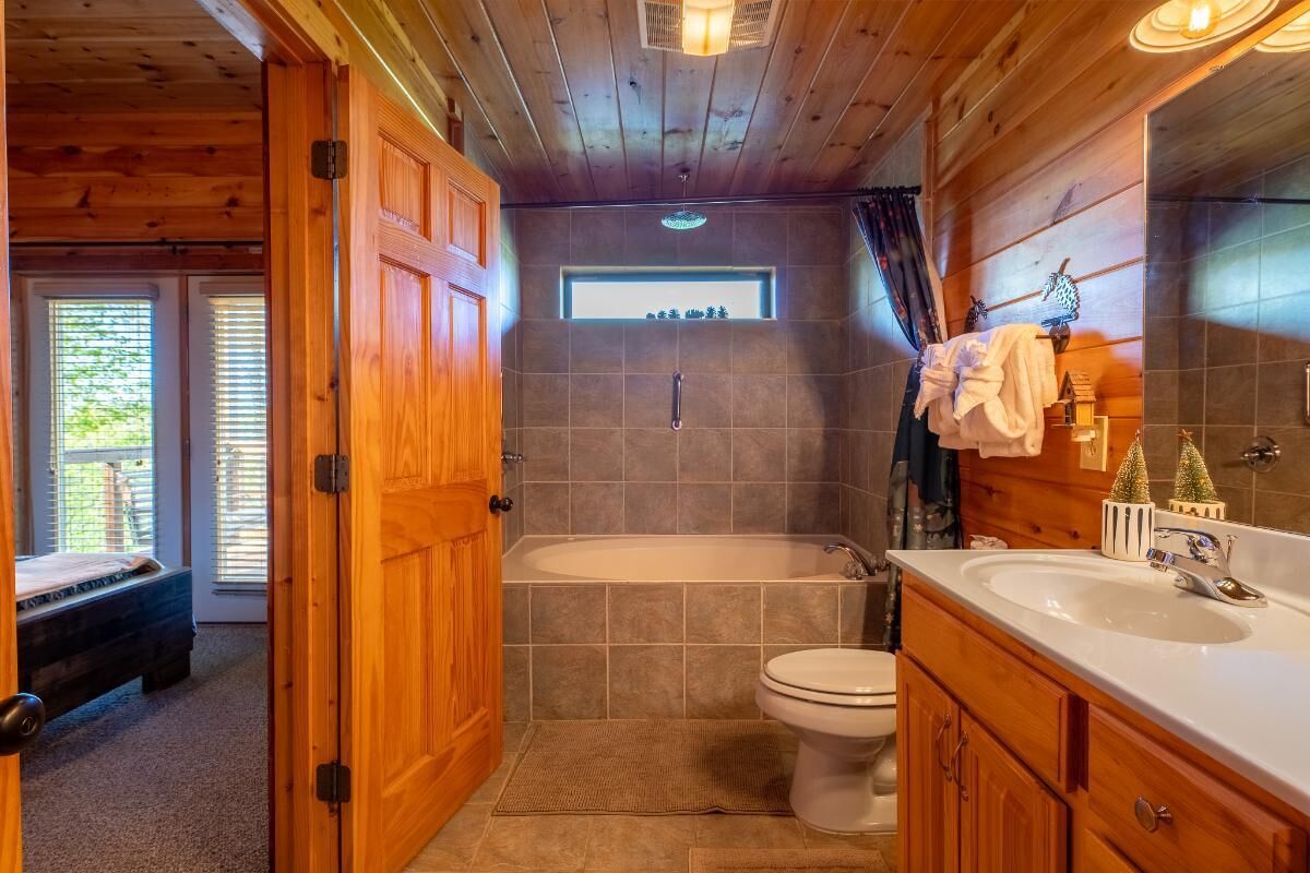 A wooden cabin bathroom with a bathtub, toilet, and vanity.