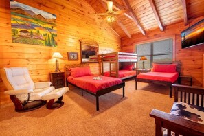 A cabin interior with a wooden ceiling, two beds with red bedding, a white leather chair, a wooden bench, a lamp, and a painting on the wall. - Psalm 2705 (Sevierville)