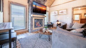 A cozy living room with a stone fireplace, a flat-screen TV mounted on the wall, and a comfortable seating area with a sofa and armchairs. - Suite Retreat (Pigeon Forge)