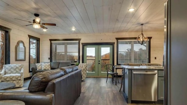 A modern kitchen with a built-in dishwasher, a dining area with a table and chairs, and a seating area with a sofa and armchairs. - Bluemoon Ridge (Pigeon Forge)