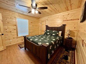Ein Schlafzimmer einer Holzhütte mit Bett, Deckenventilator, Fenster und Nachttisch.