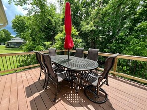 Eine Terrasse mit einem runden Tisch, Stühlen, einem roten Sonnenschirm und einem Holgitter.