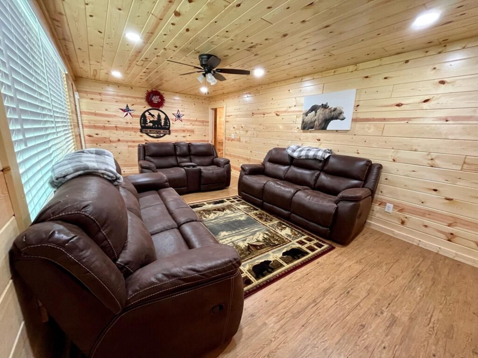 Ein Holzblockhaus-Innenraum mit einem Ecksofa, einem Deckenventilator und einem Bären-Teppich.
