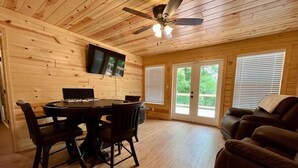 Un intérieur en bois comprenant une table à manger, des chaises, un canapé, un ventilateur de plafond et un téléviseur fixé au mur.