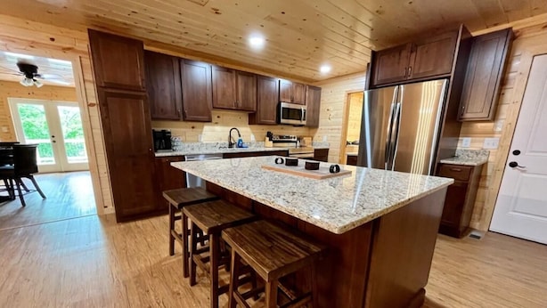 Une cuisine avec des meubles en bois, des plans de travail en granit, un îlot central avec des tabourets, un réfrigérateur et un four à micro-ondes.