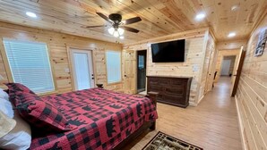 Une chambre à coucher dans un chalet en bois, avec un lit, une commode, un téléviseur et une cheminée.