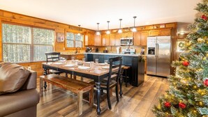 A modern kitchen with wooden cabinets, a central island, stainless steel appliances, and a dining area with a bench. - Birdies and Bearcubs (Pigeon Forge)