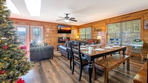 A cozy cabin interior with a dining area, a fireplace, and a Christmas tree. - Birdies and Bearcubs (Pigeon Forge)