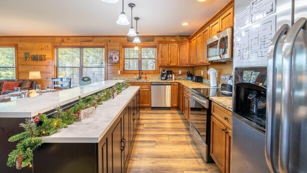 A modern kitchen with wooden cabinets, stainless steel appliances, and a central island with a decorative garland. - Birdies and Bearcubs (Pigeon Forge)