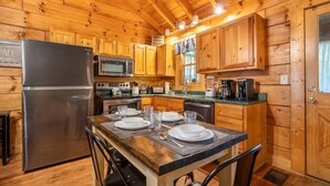 Une cuisine aménagée dans le style d’un chalet en bois, équipée d’un réfrigérateur, d’un four à micro-ondes et d’une table à manger pour quatre personnes.