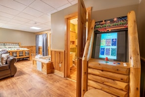 Een houten cabin met een houten bed, een houten bureau met een computer, en een houten deur naar een badkamer.