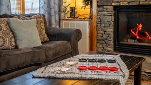 Un salon chaleureux avec une cheminée, un canapé et une table basse sur laquelle sont posées des jeux de cartes.