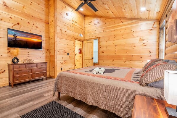 A wooden cabin bedroom with a bed, dresser, television, and a ceiling fan. - Nestled Inn (Sevierville)