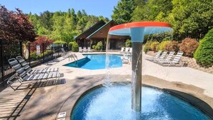A swimming pool with a water fountain, lounge chairs, and a building in the background. - Z - Bear Ridge (Gatlinburg)