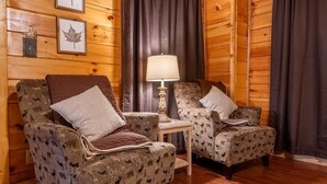 A log cabin interior with two patterned armchairs, a small table, and a lamp. - Timber Tails (Sevierville)